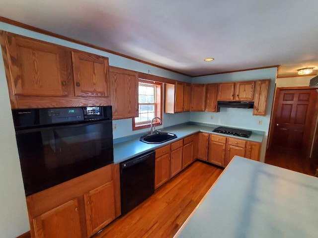 kitchen featuring brown cabinets, light wood finished floors, a sink, under cabinet range hood, and black appliances