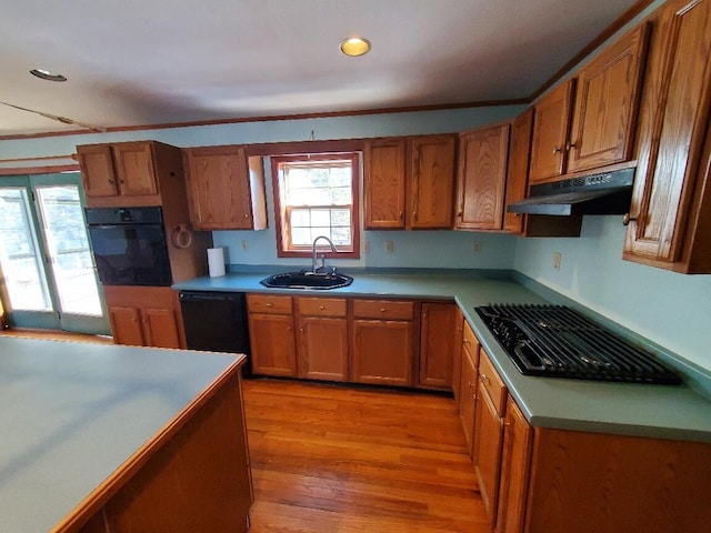 kitchen with under cabinet range hood, a sink, light countertops, black appliances, and brown cabinetry