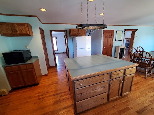 kitchen with a center island, light wood finished floors, brown cabinetry, freestanding refrigerator, and black microwave