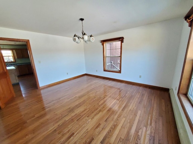 unfurnished room with hardwood / wood-style floors, baseboard heating, a sink, a chandelier, and baseboards