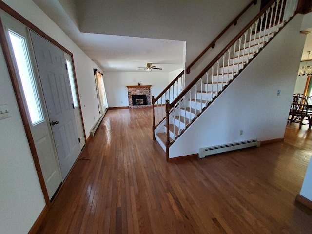 entrance foyer with baseboards, stairway, wood finished floors, a brick fireplace, and a baseboard heating unit