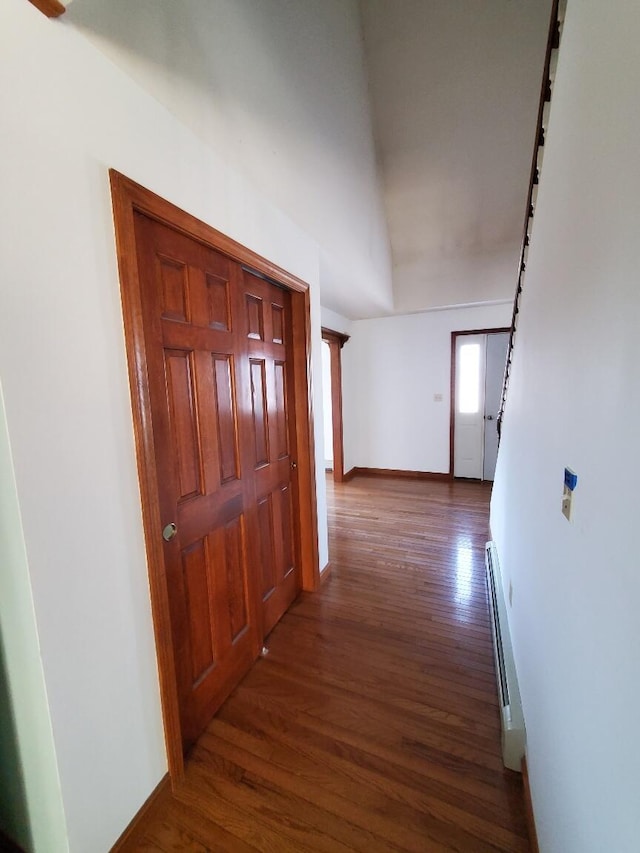 corridor with a baseboard heating unit, dark wood-type flooring, and baseboards