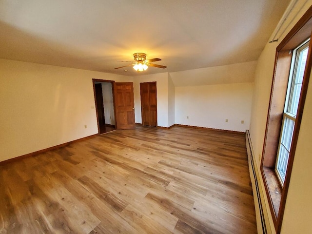 spare room with a baseboard heating unit, light wood-style floors, baseboards, and a ceiling fan