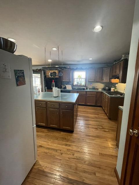 kitchen featuring freestanding refrigerator, under cabinet range hood, light countertops, light wood-style floors, and stainless steel gas cooktop