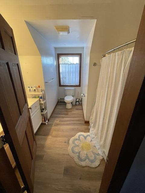 bathroom featuring baseboards, toilet, wood finished floors, baseboard heating, and vanity