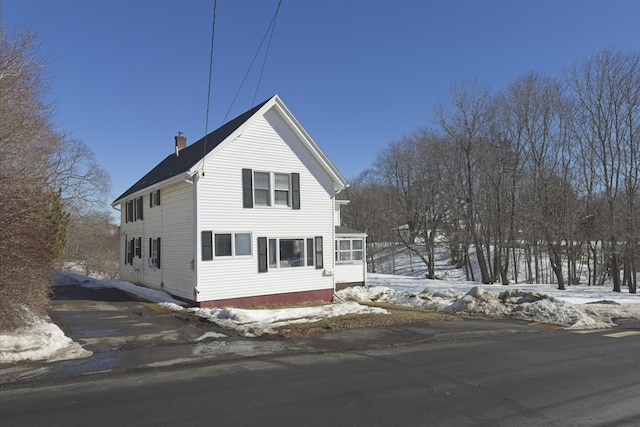 view of snowy exterior with driveway and a chimney