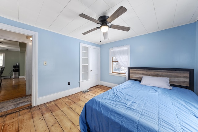 bedroom with a ceiling fan, a baseboard radiator, baseboards, and hardwood / wood-style flooring