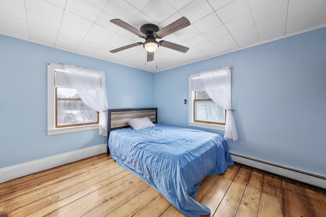 bedroom with a ceiling fan, baseboards, a baseboard heating unit, and hardwood / wood-style floors