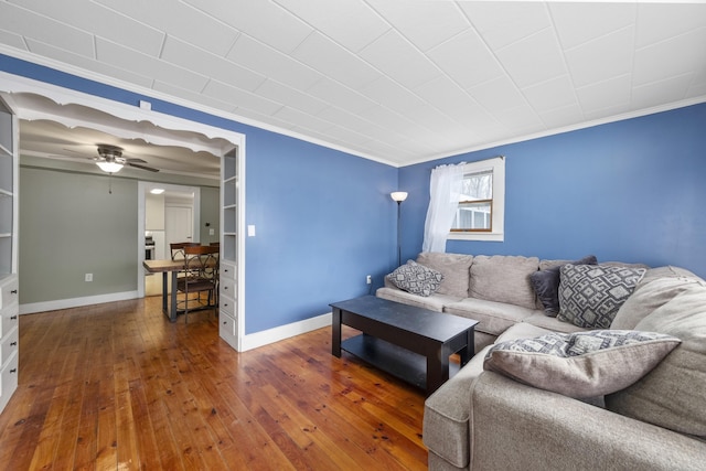 living room with wood-type flooring, crown molding, baseboards, and a ceiling fan