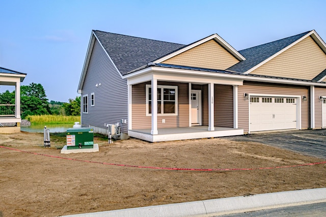 view of front facade featuring covered porch, driveway, roof with shingles, and a garage