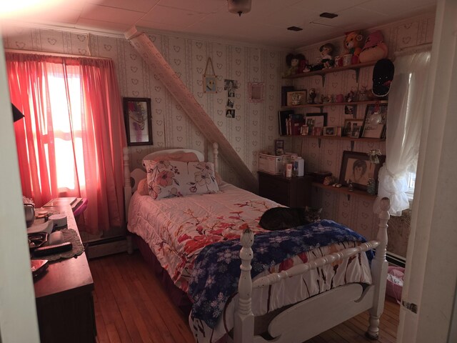 bedroom with a baseboard heating unit, crown molding, hardwood / wood-style floors, and wallpapered walls