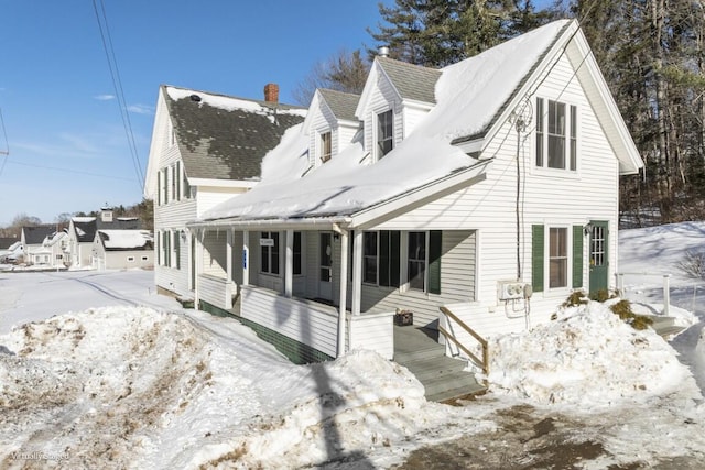 snow covered house with a shingled roof and a porch