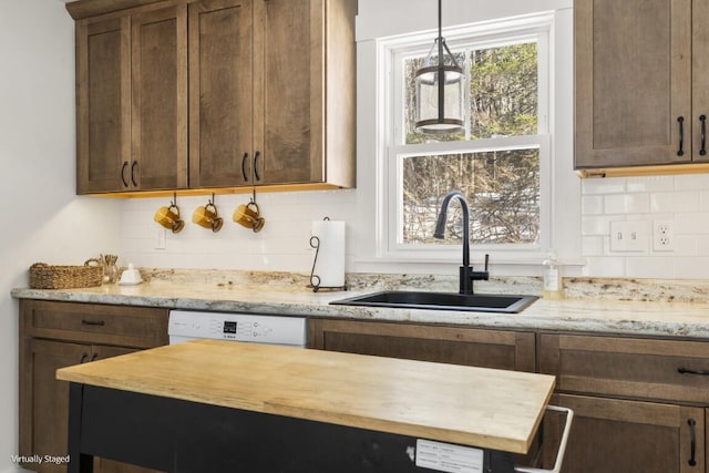 kitchen with tasteful backsplash, white dishwasher, a sink, and decorative light fixtures