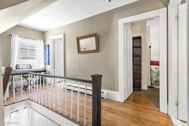 corridor featuring a baseboard heating unit, baseboards, an upstairs landing, and light wood finished floors