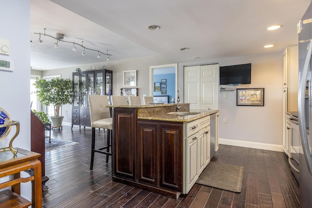 kitchen featuring a breakfast bar, dark wood-style flooring, a sink, light stone countertops, and baseboards