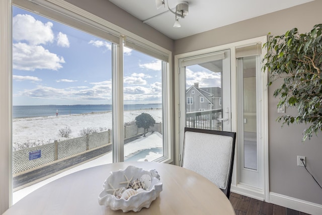 dining room with a water view, baseboards, a beach view, and dark wood-type flooring