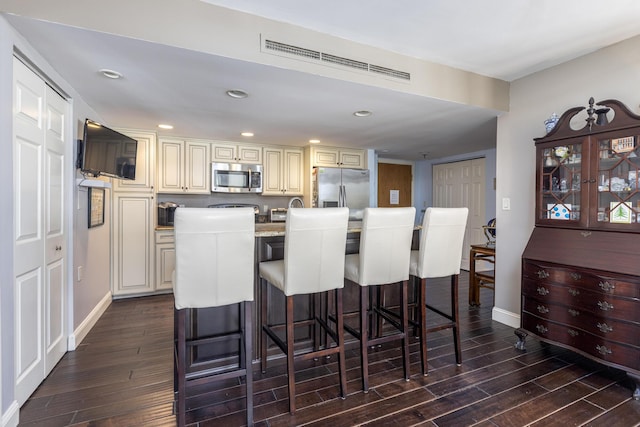 kitchen featuring dark wood-style floors, a breakfast bar area, recessed lighting, cream cabinets, and appliances with stainless steel finishes