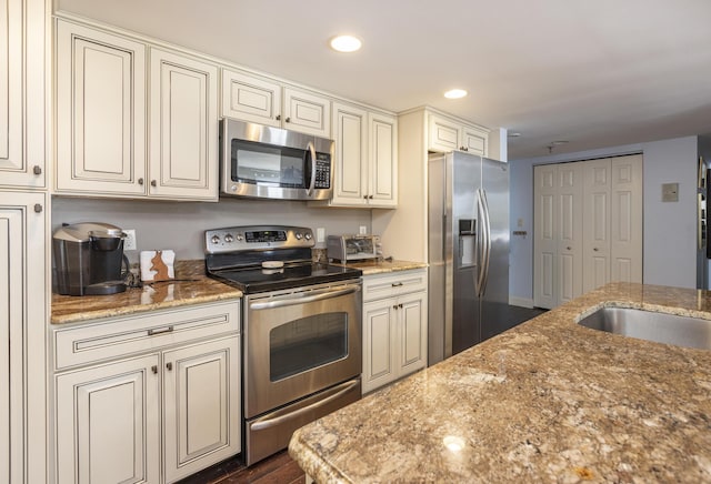 kitchen with cream cabinets, recessed lighting, appliances with stainless steel finishes, light stone countertops, and dark wood finished floors