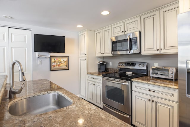 kitchen featuring a toaster, cream cabinets, stainless steel appliances, stone counters, and a sink