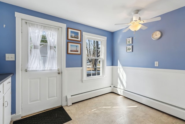 doorway featuring baseboard heating, wainscoting, and a ceiling fan