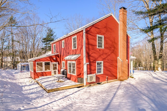 snow covered property with ac unit and a chimney