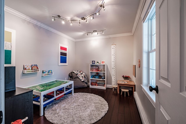 playroom with a baseboard heating unit, dark wood-type flooring, rail lighting, and crown molding