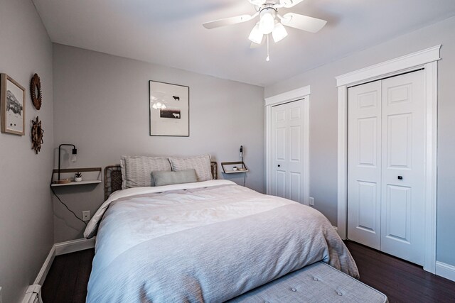 bedroom with dark wood-type flooring, a ceiling fan, baseboards, and two closets