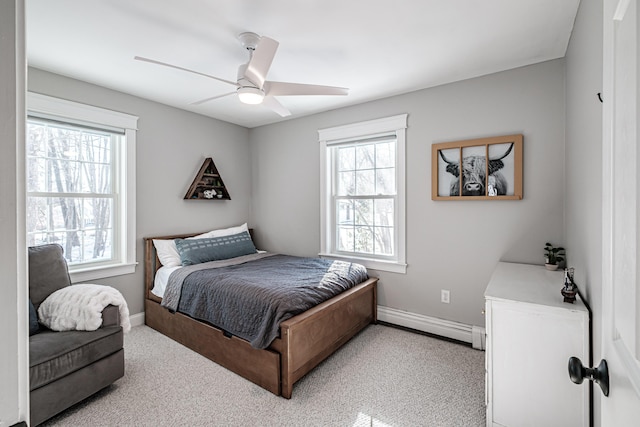 bedroom with a baseboard heating unit, light carpet, a ceiling fan, and baseboards