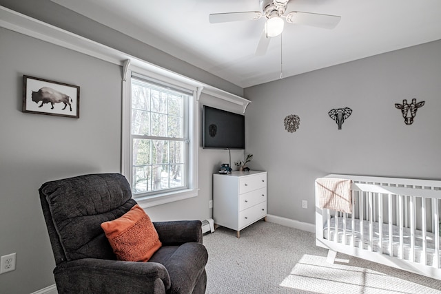 bedroom featuring a crib, baseboards, a ceiling fan, light colored carpet, and a baseboard heating unit