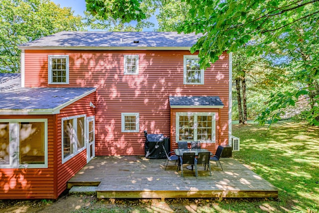 back of property with outdoor dining area, a yard, a deck, and roof with shingles