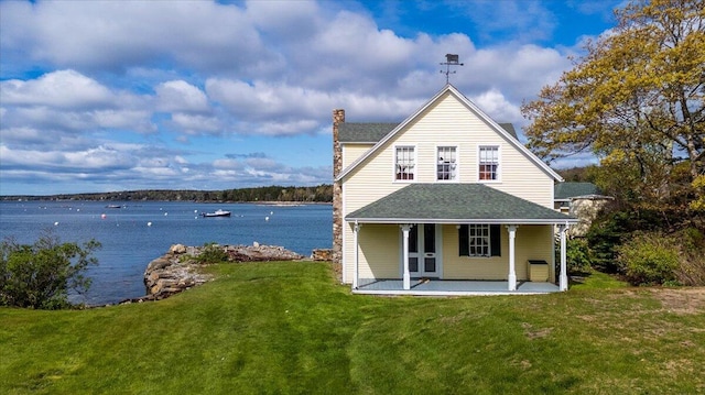 back of property with a chimney, a lawn, a water view, and a shingled roof