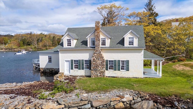view of front of home featuring a water view, a chimney, roof with shingles, and a front yard