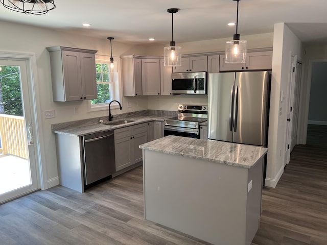 kitchen featuring gray cabinets, a sink, wood finished floors, appliances with stainless steel finishes, and light stone countertops