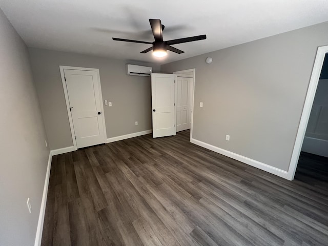 unfurnished bedroom featuring a wall unit AC, a ceiling fan, baseboards, dark wood-type flooring, and a barn door