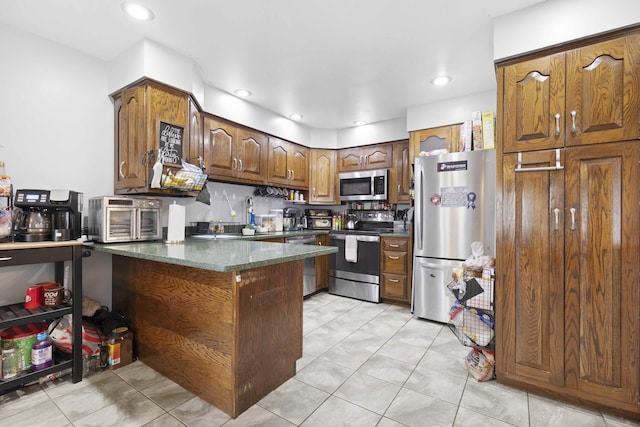 kitchen featuring dark stone counters, appliances with stainless steel finishes, a toaster, a peninsula, and brown cabinetry