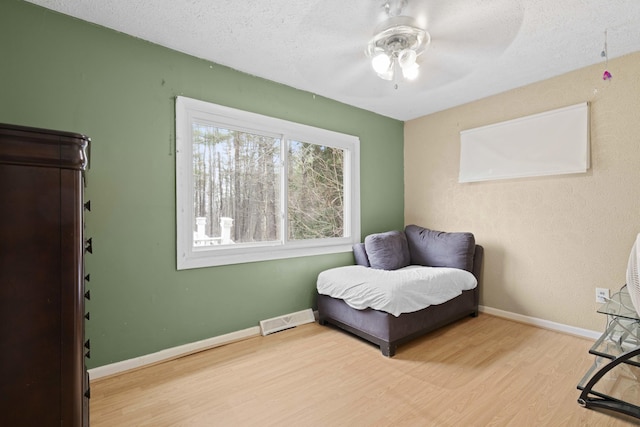 living area featuring a textured ceiling, visible vents, baseboards, wood finished floors, and a ceiling fan