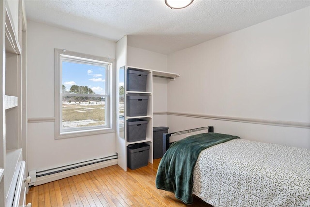 bedroom featuring a baseboard heating unit, wood-type flooring, and a textured ceiling