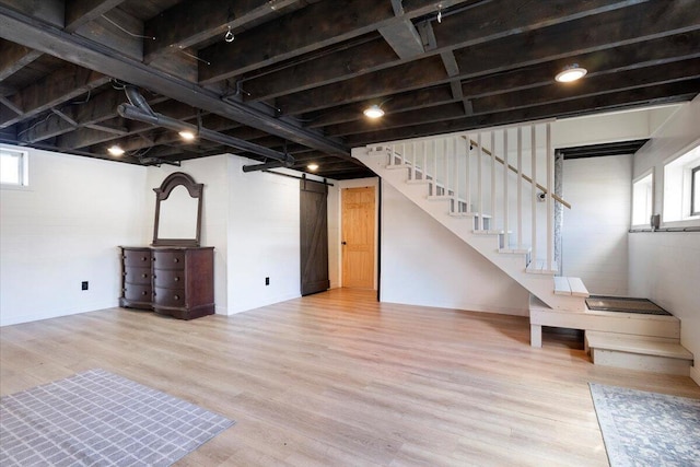 basement featuring a wealth of natural light, a barn door, wood finished floors, and stairs