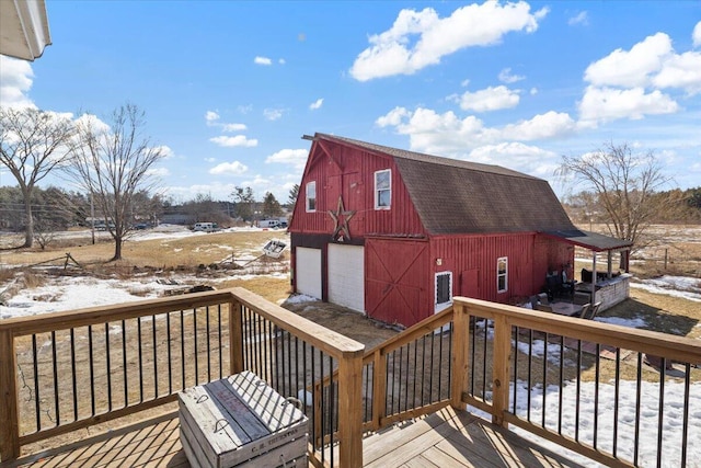 snow covered deck featuring a barn, an outbuilding, and a garage