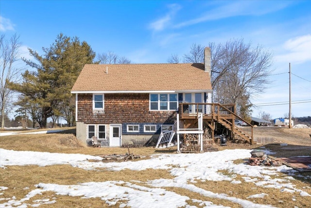 snow covered property with a chimney, stairway, a wooden deck, and a shingled roof