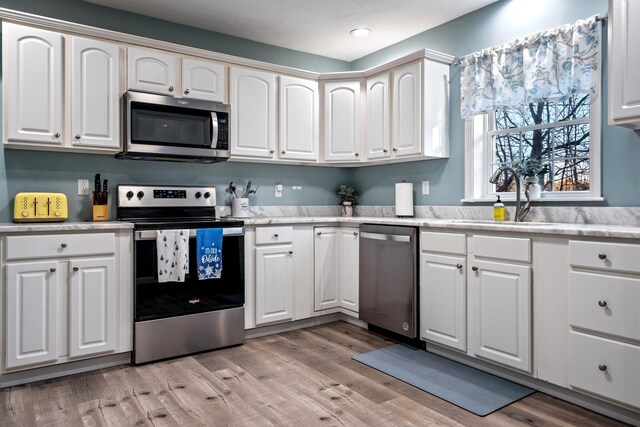 kitchen with stainless steel appliances, light countertops, white cabinets, a sink, and light wood-type flooring