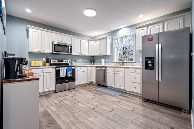 kitchen with appliances with stainless steel finishes, light countertops, a sink, and light wood finished floors