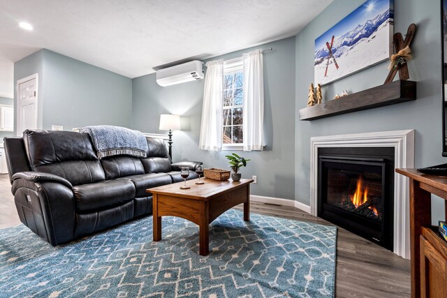 living room with a wall unit AC, baseboards, wood finished floors, and a glass covered fireplace