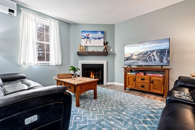 living room featuring a warm lit fireplace, a wall mounted air conditioner, baseboards, and wood finished floors