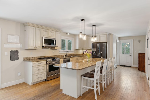 kitchen with light stone counters, appliances with stainless steel finishes, light wood-type flooring, and cream cabinetry