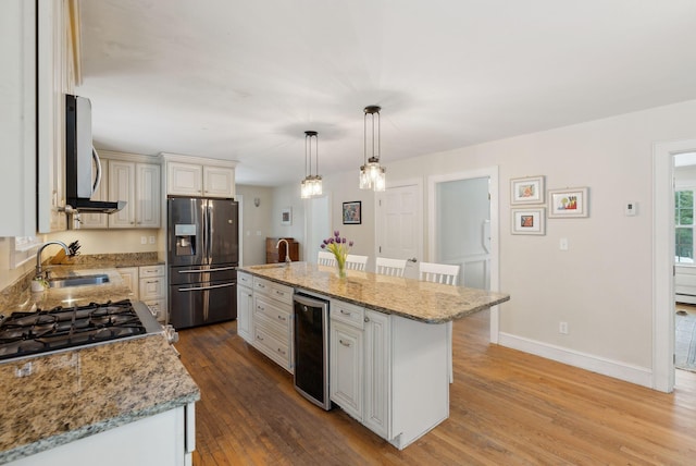 kitchen with wine cooler, appliances with stainless steel finishes, a sink, wood finished floors, and baseboards