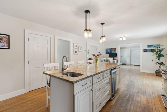 kitchen featuring a kitchen island with sink, hardwood / wood-style flooring, beverage cooler, a breakfast bar, and a sink