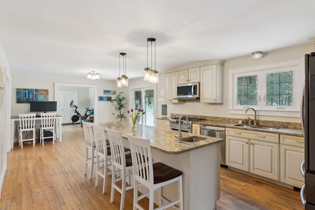 kitchen with stainless steel appliances, a sink, light wood-style floors, cream cabinetry, and light stone countertops