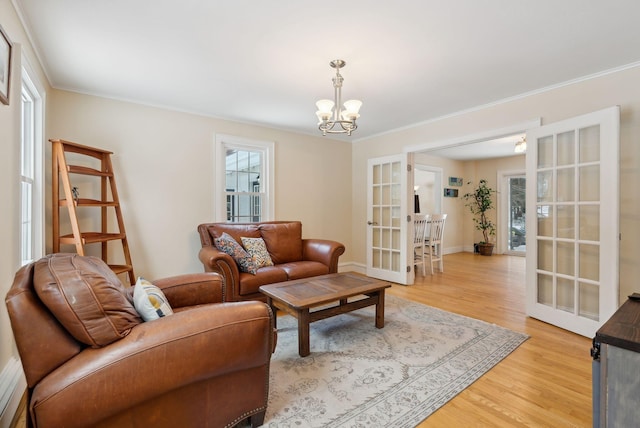 living room featuring french doors, crown molding, a notable chandelier, light wood-style floors, and baseboards