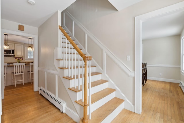 stairs with a baseboard heating unit, wood-type flooring, a decorative wall, and baseboards